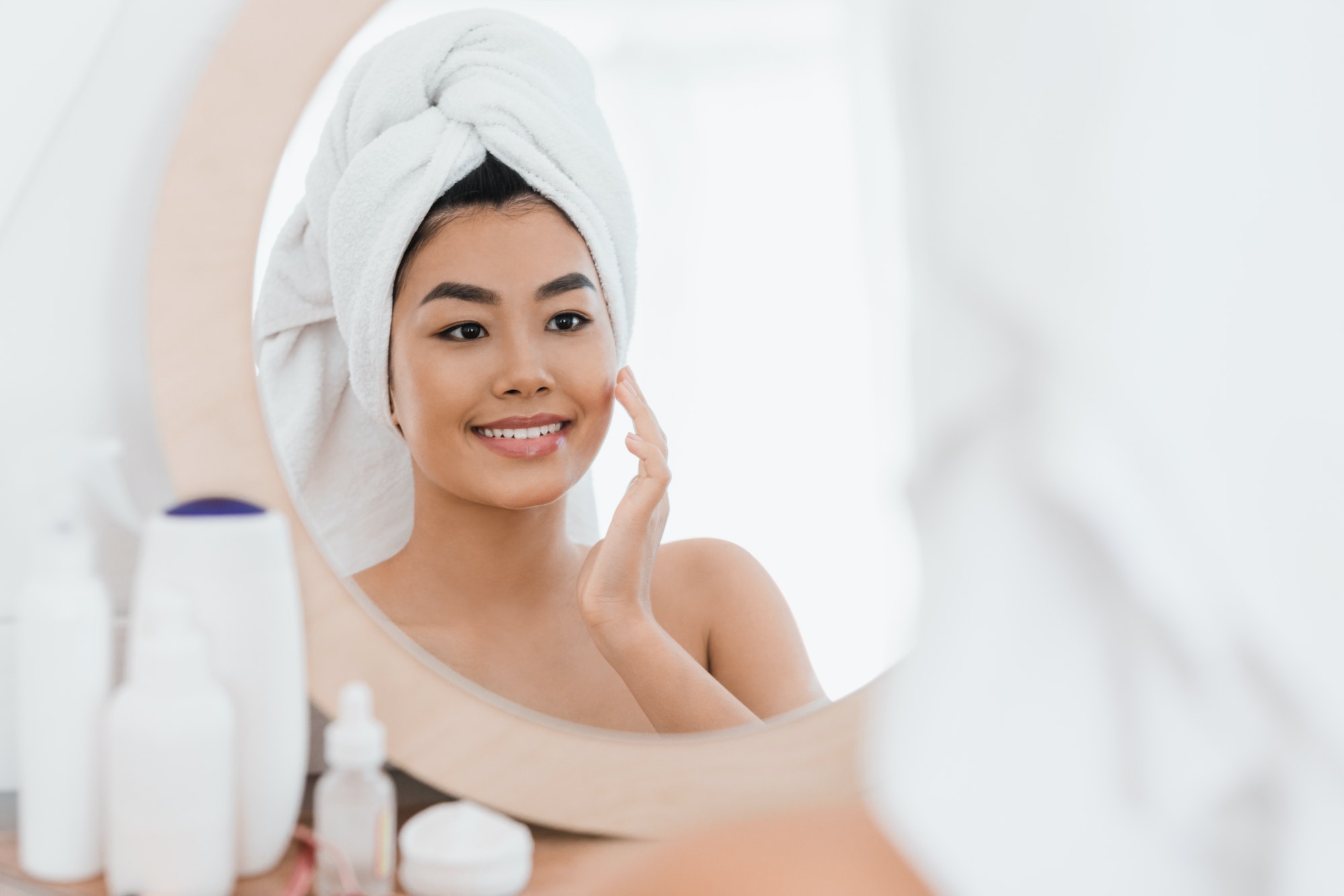 Cheerful asian young woman applying beauty product