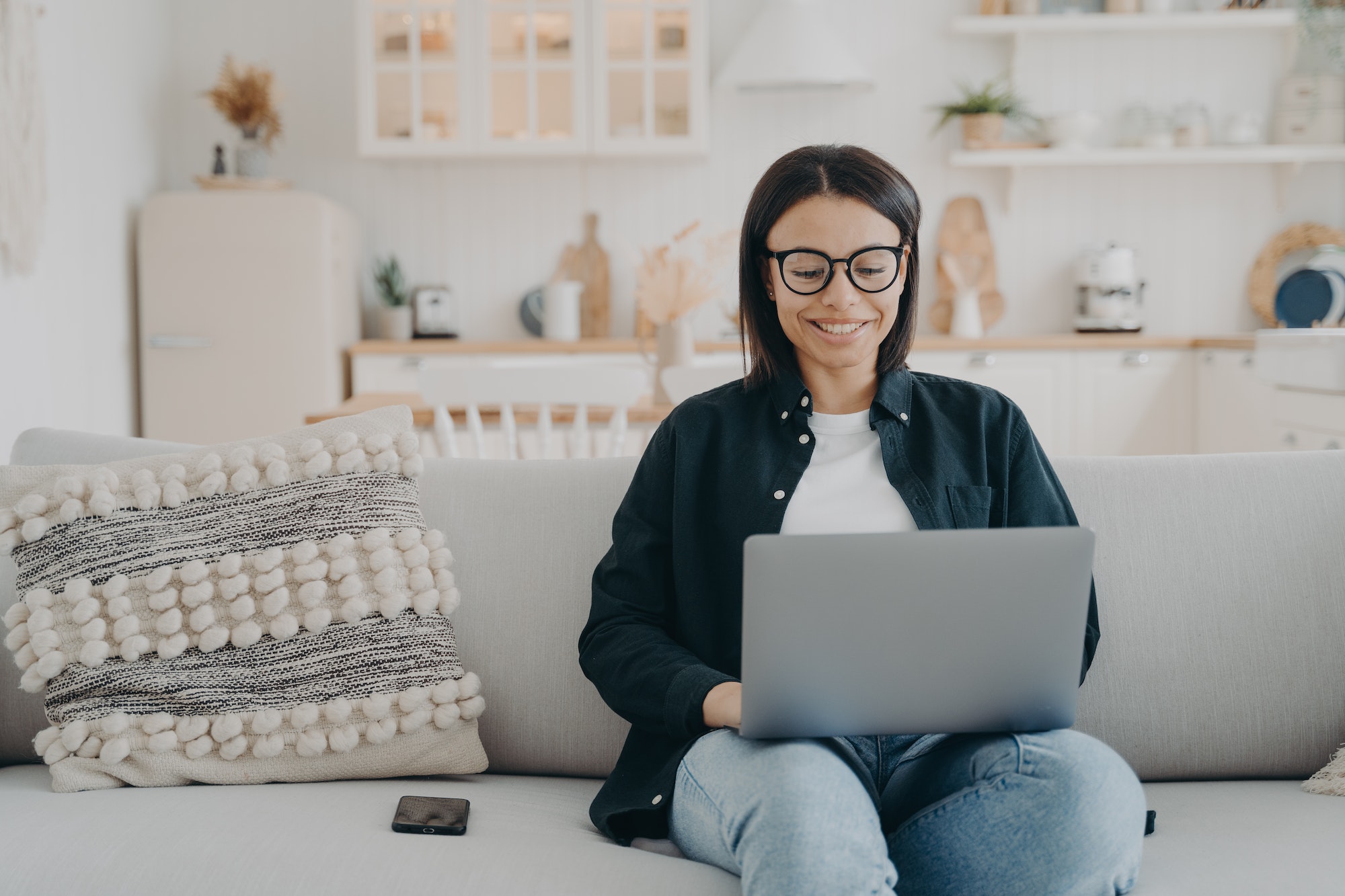 Smiling female working on laptop, shopping in online store, sitting on cozy couch at home. Ecommerce